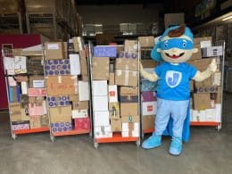 Mascotte Stichting Jarige Job staat voor rolcontainers vol gedoneerde cadeaus